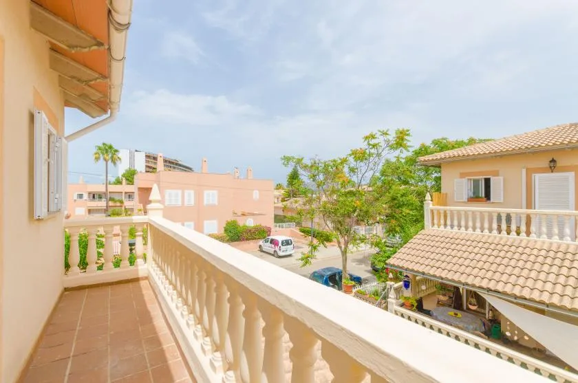 Un balcón soleado da a casas cercanas y árboles frondosos.