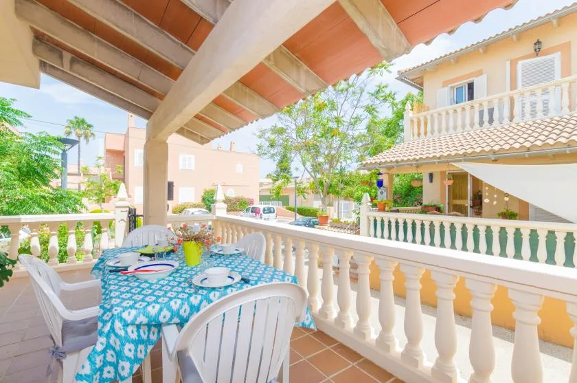 Una terraza cubierta con comedor da a un patio con vegetación y edificios cercanos.