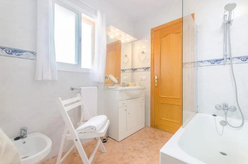 Un baño luminoso con lavabo, bañera y silla plegable blanca.