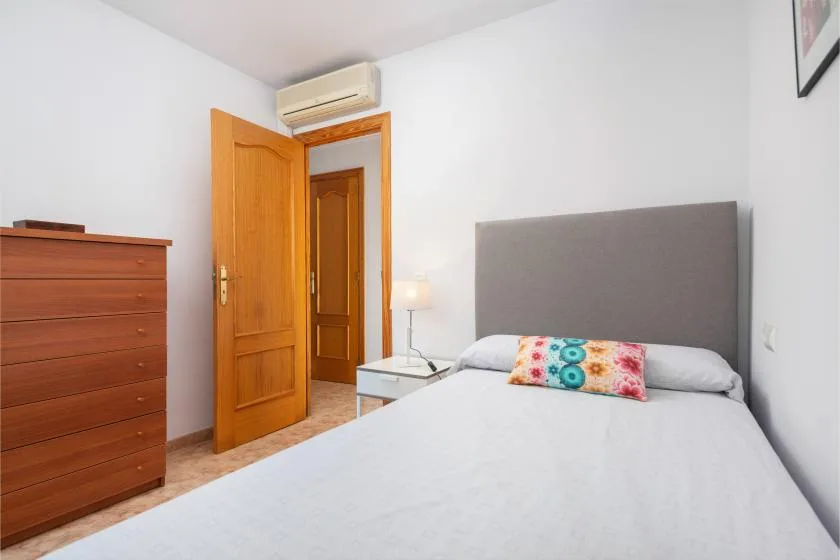 Un dormitorio con una cama, una cómoda de madera y una puerta abierta.