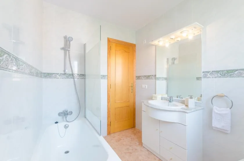 Un baño luminoso con bañera, ducha y lavabo bajo un espejo grande.