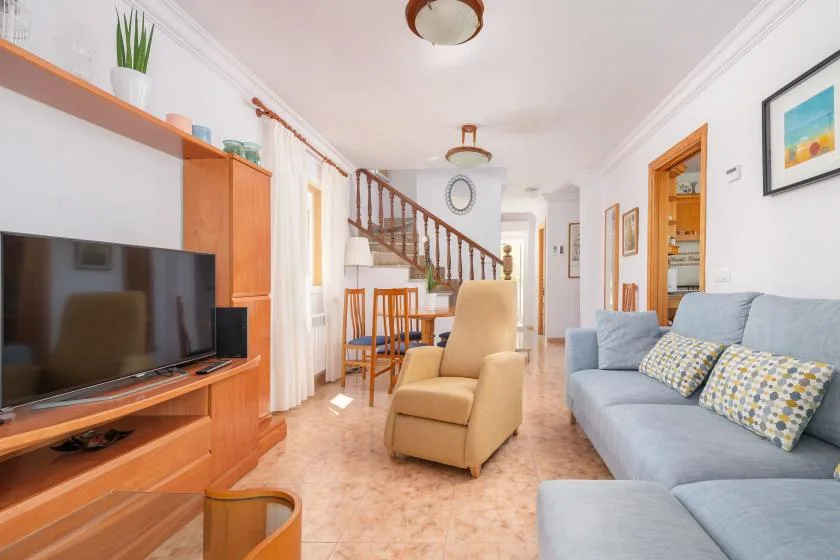Una sala de estar con televisor, sillón y sofá junto a una escalera.