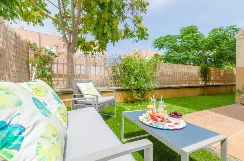A garden patio with outdoor seating, a low table, and green lawn.