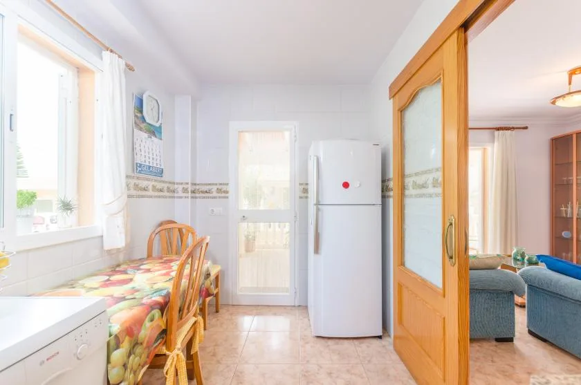 Una cocina luminosa con una mesa de comedor junto a una puerta acristalada y un refrigerador.