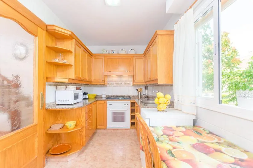 Una cocina luminosa con armarios de madera, encimeras blancas y un mantel colorido.