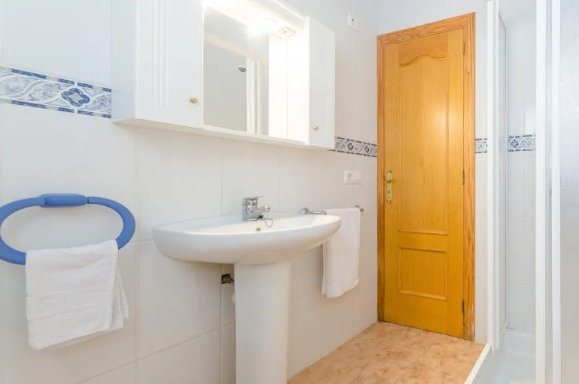 Un baño luminoso con lavabo de pedestal, espejo de pared y puerta de madera.