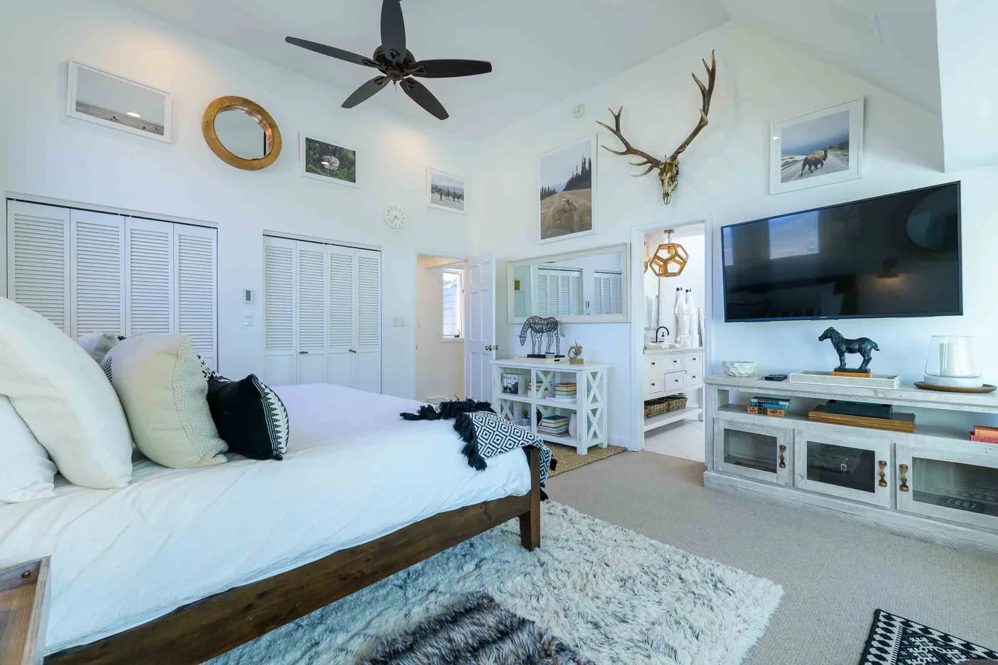 Un dormitorio luminoso con una cama, un televisor montado en la pared y un ventilador de techo.