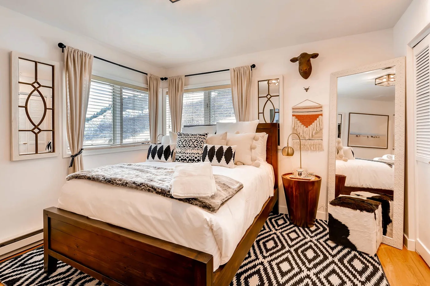Dormitorio luminoso con cama, alfombra estampada y ventanas con cortinas.
