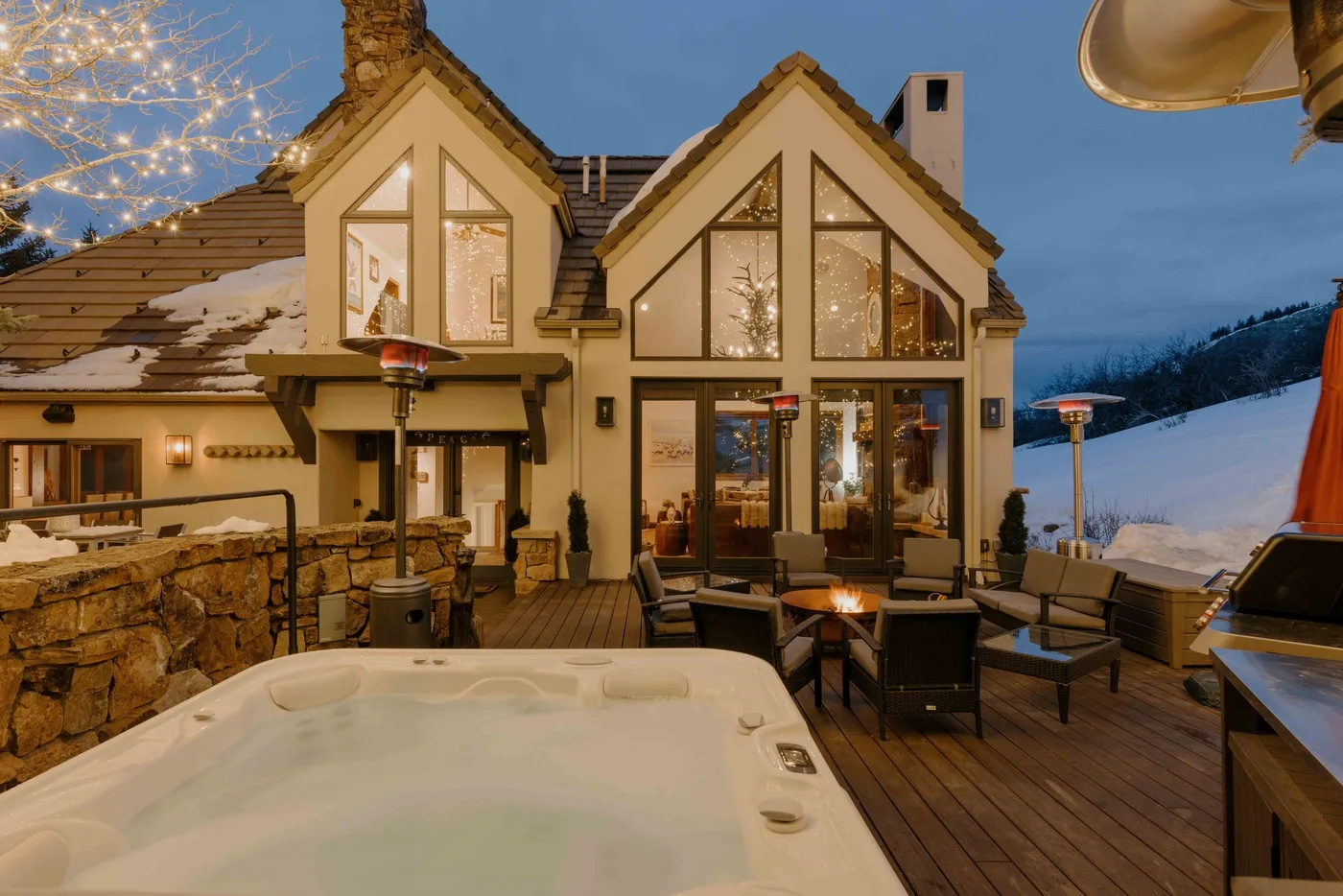 Exterior de un chalet al anochecer, con una bañera de hidromasaje y asientos en la terraza.