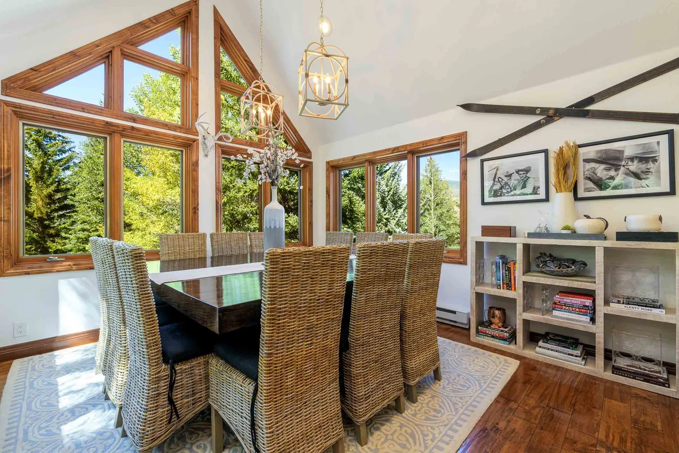 Un comedor con asientos tejidos, grandes ventanas y un mueble bajo con estantes.
