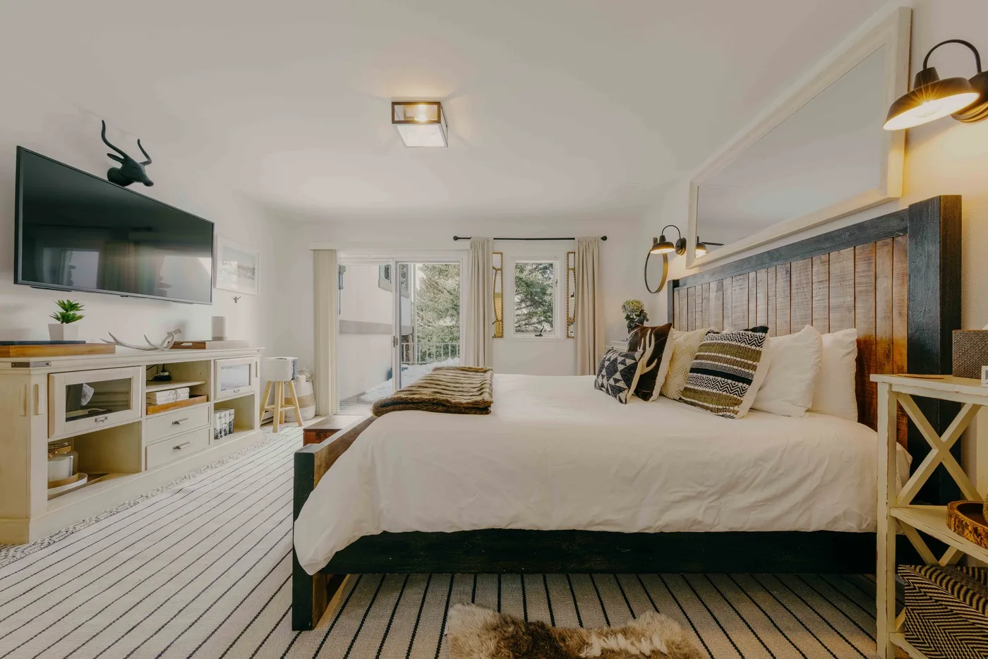 Un dormitorio luminoso con una cama grande, suelo a rayas y un televisor.