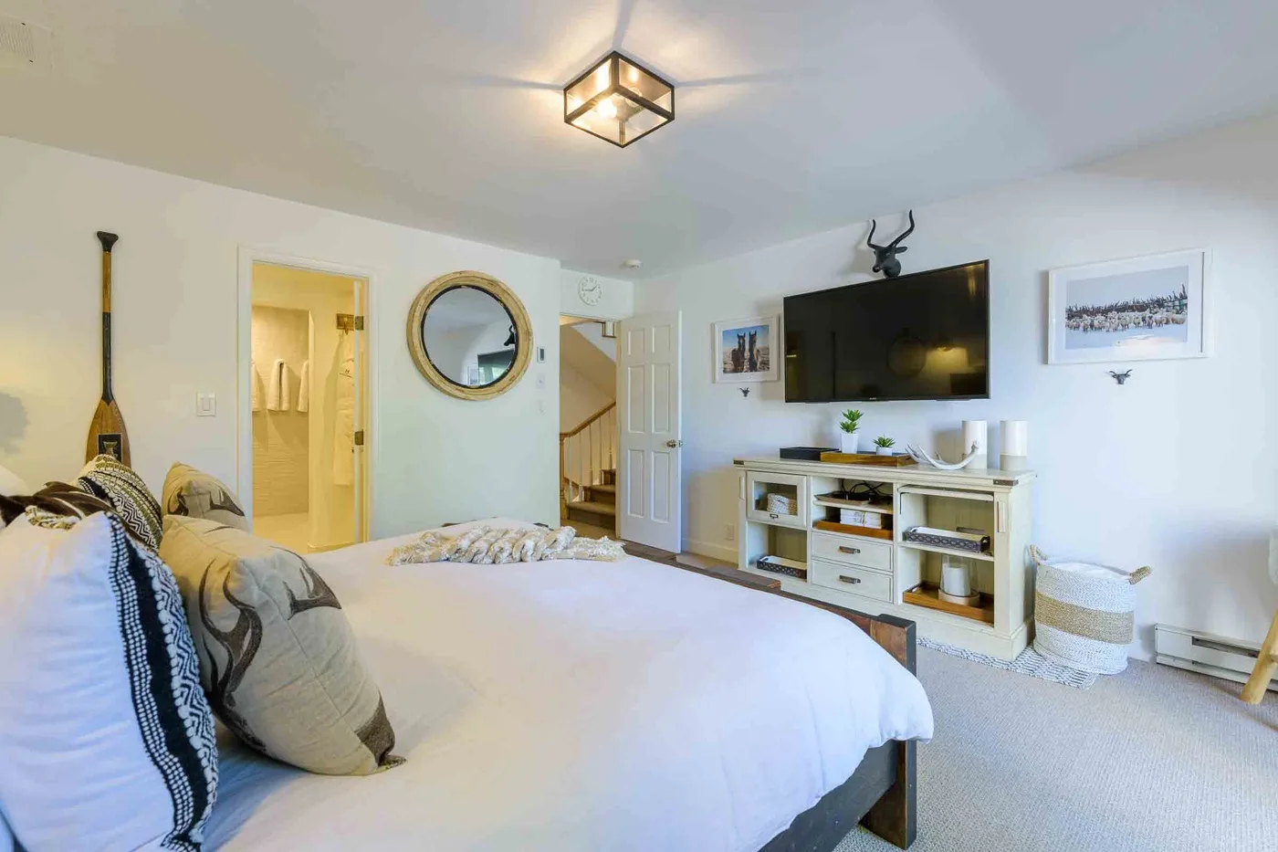 Dormitorio luminoso con una cama grande y un televisor en la pared.