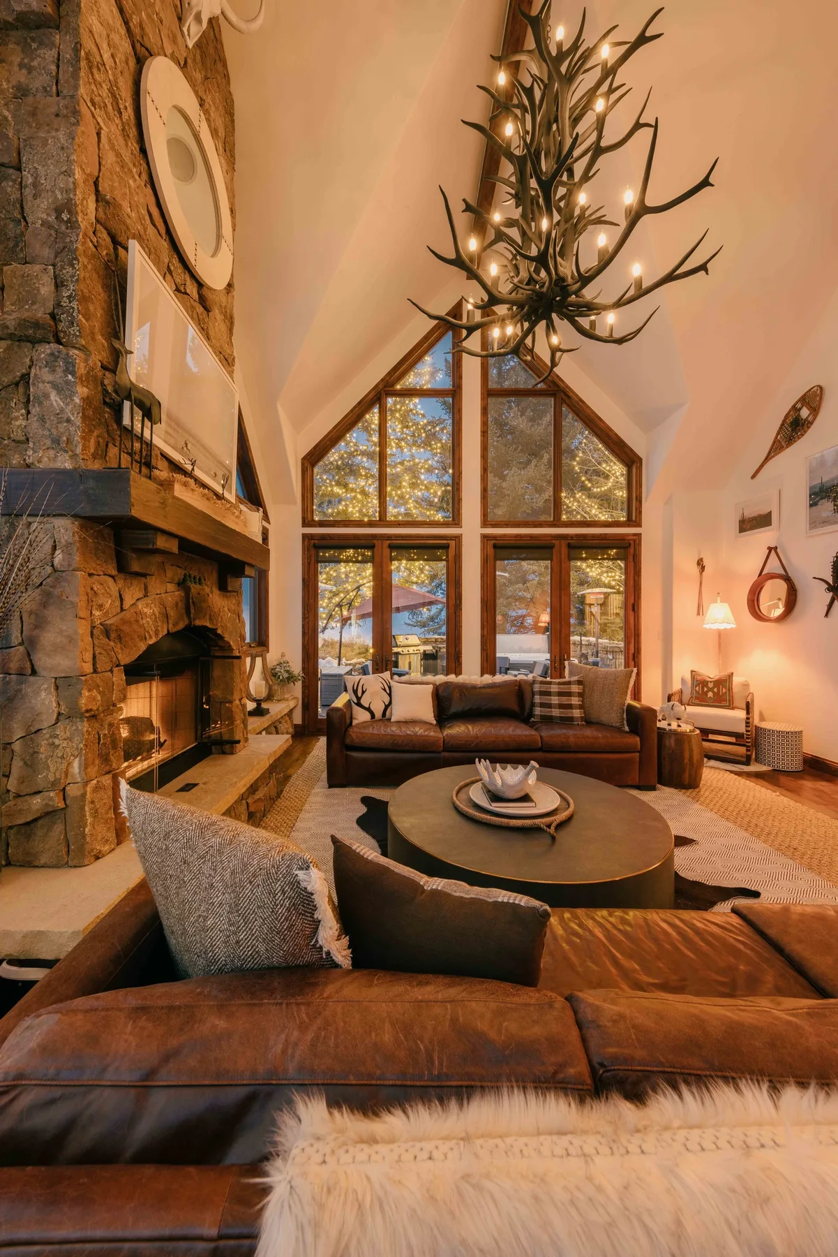 Una acogedora sala de estar con chimenea de piedra, asientos y ventanas altas.
