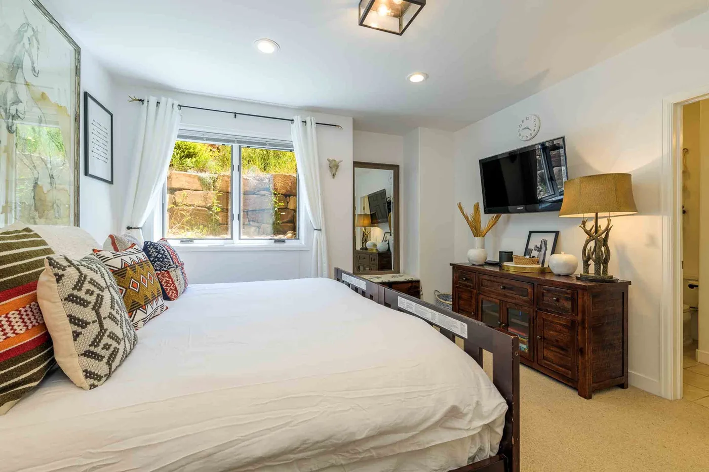 Un dormitorio luminoso con una cama grande, una ventana y una cómoda de madera.