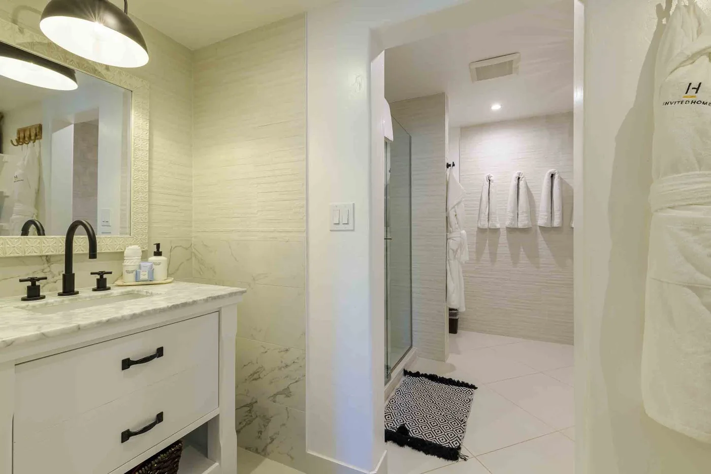Un tocador de baño luminoso da a una zona de ducha revestida con azulejos y toallas colgadas.