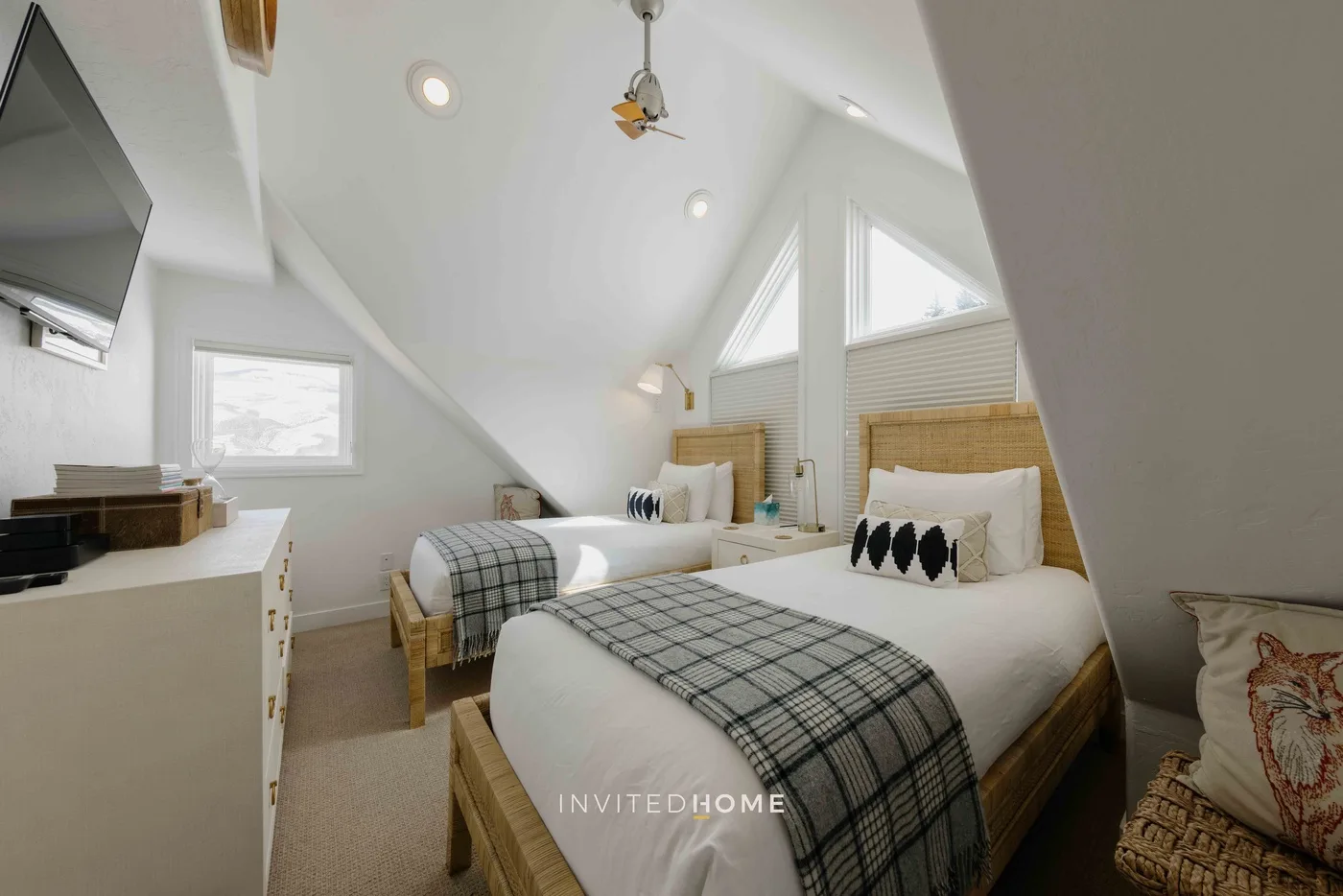 Un dormitorio luminoso con dos camas bajo un techo inclinado y tragaluces.