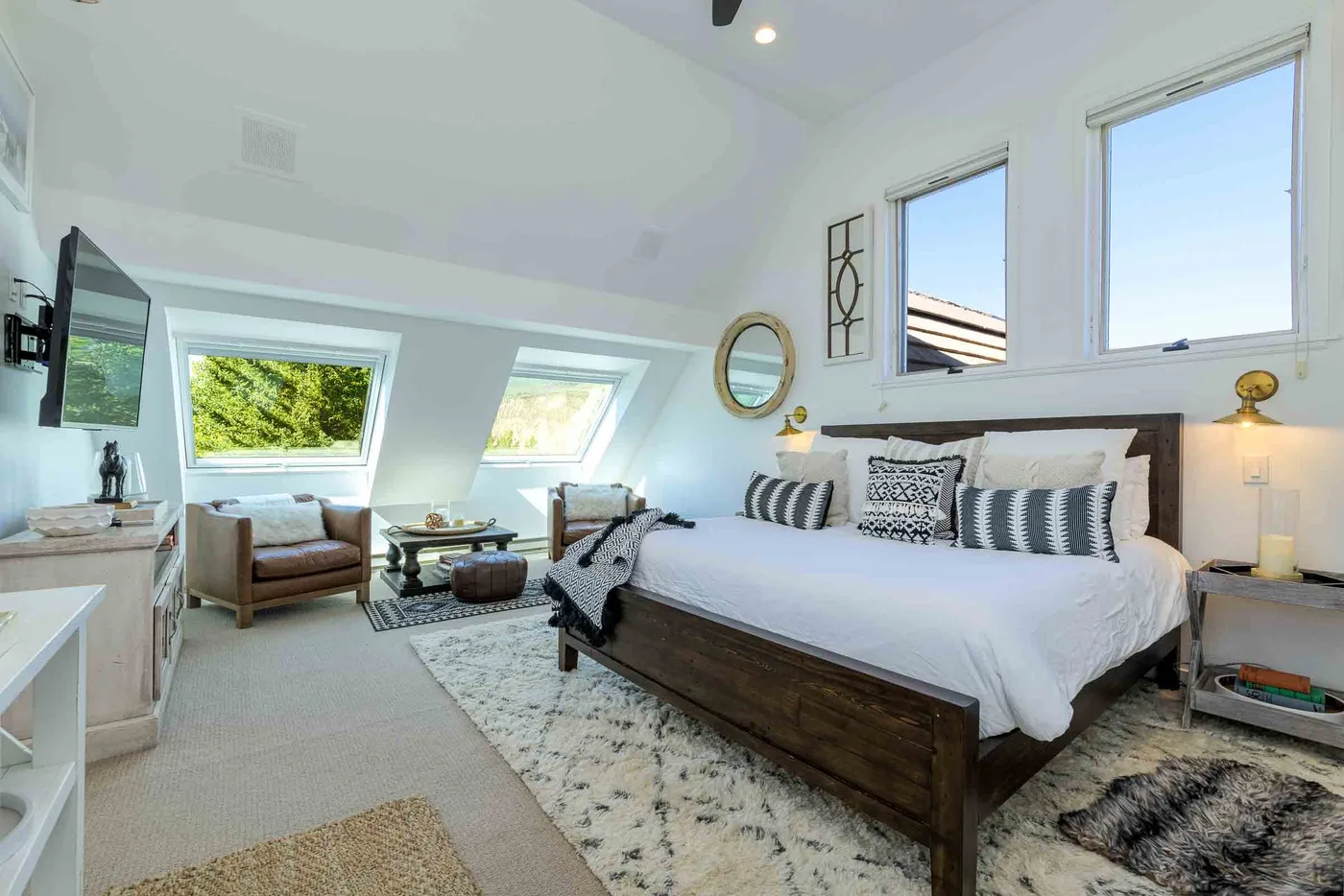 Un dormitorio luminoso con una cama grande, asientos y ventanas.