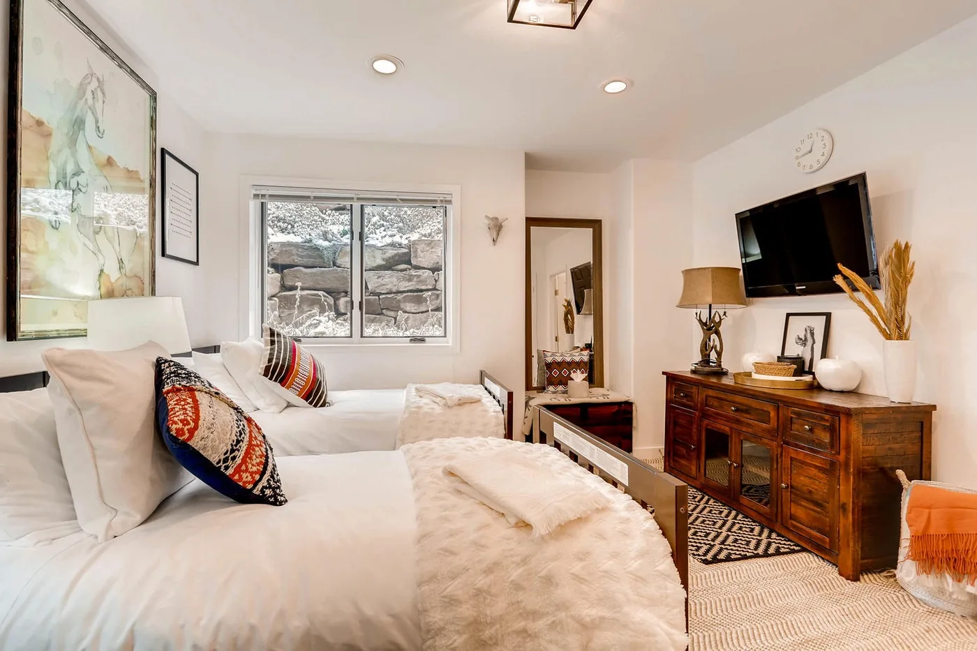 Un dormitorio con ropa de cama blanca, una ventana y una cómoda de madera.