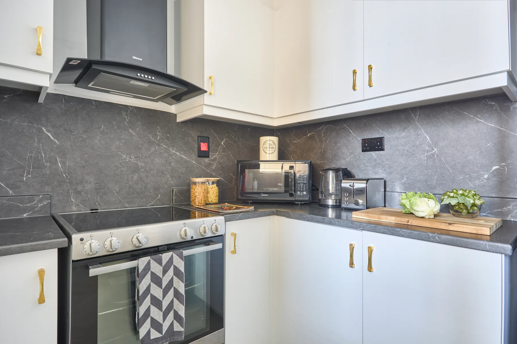 Una cocina luminosa con gabinetes blancos, un salpicadero oscuro y electrodomésticos sobre la encimera.