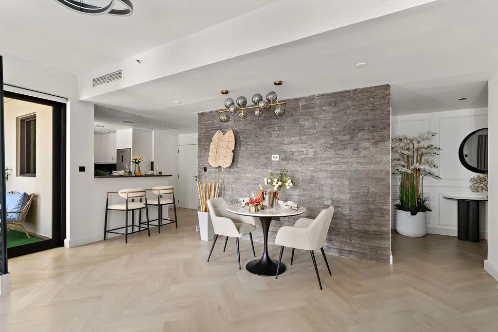 Un comedor luminoso con una mesa redonda junto a una pared decorativa gris.