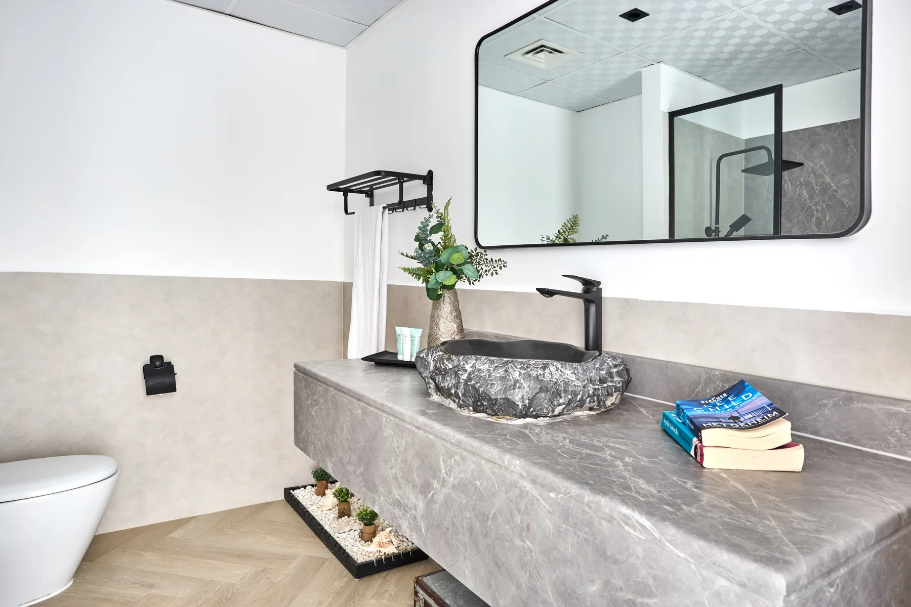 Un baño moderno cuenta con un tocador de piedra, un lavabo sobre encimera y un espejo grande.