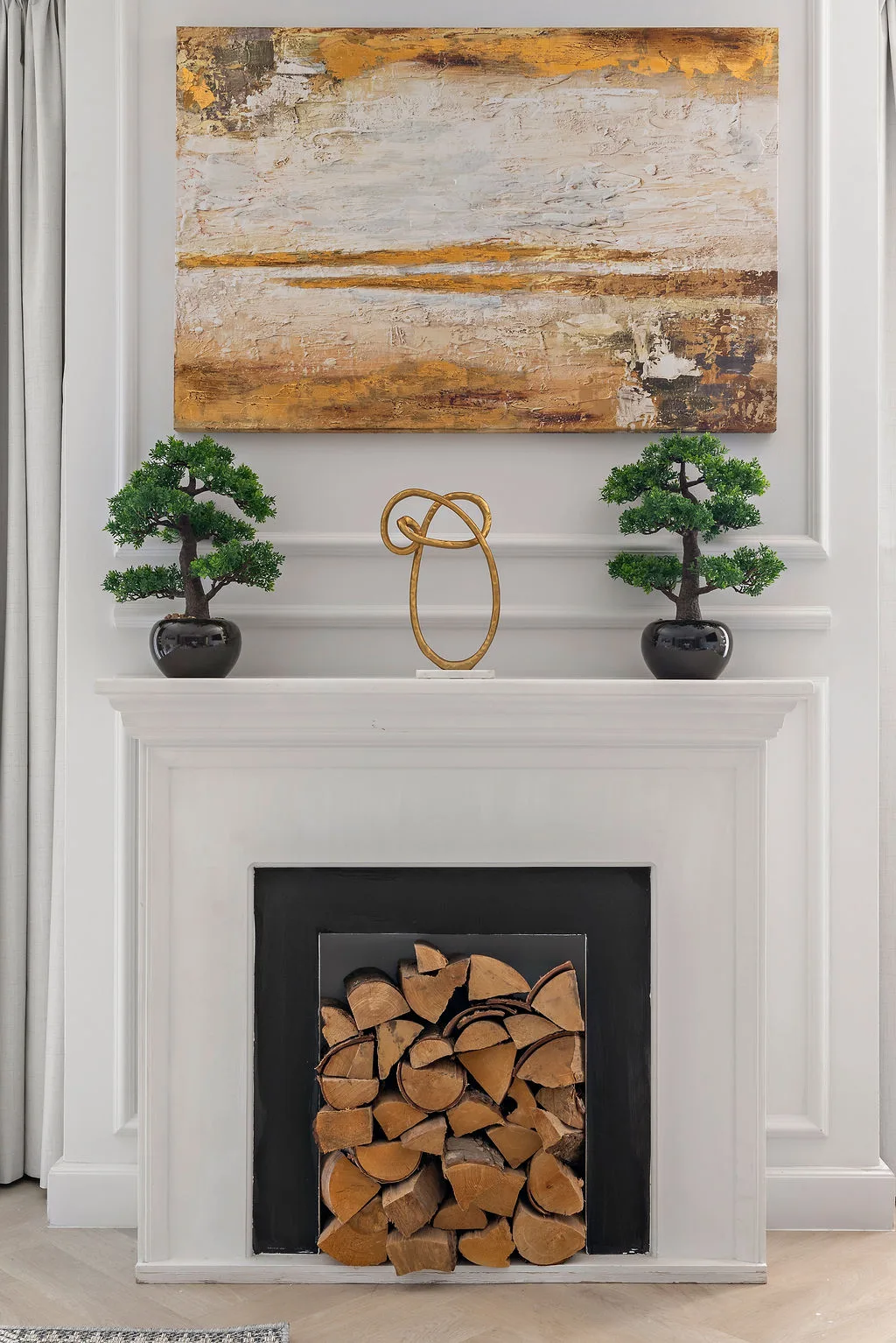 Una chimenea blanca con leños apilados debajo de una pintura abstracta.