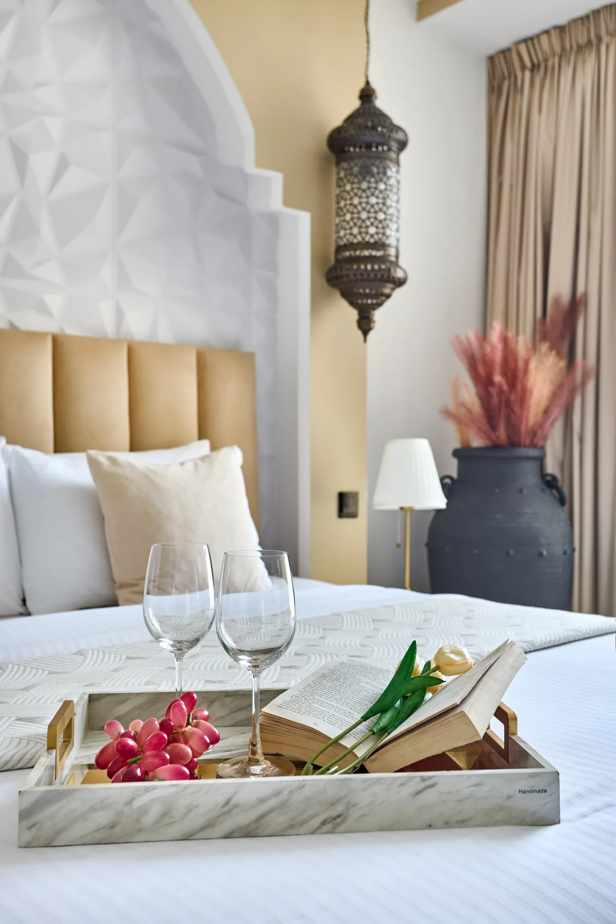 Un dormitorio ordenado presenta una lámpara decorativa y una bandeja sobre la cama.