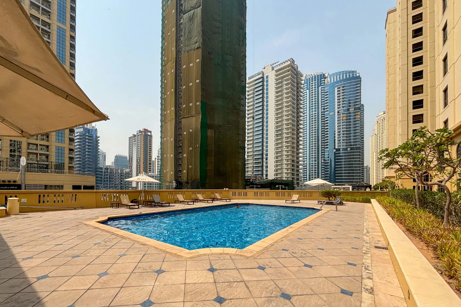 Una piscina al aire libre está en una terraza pavimentada entre edificios altos.