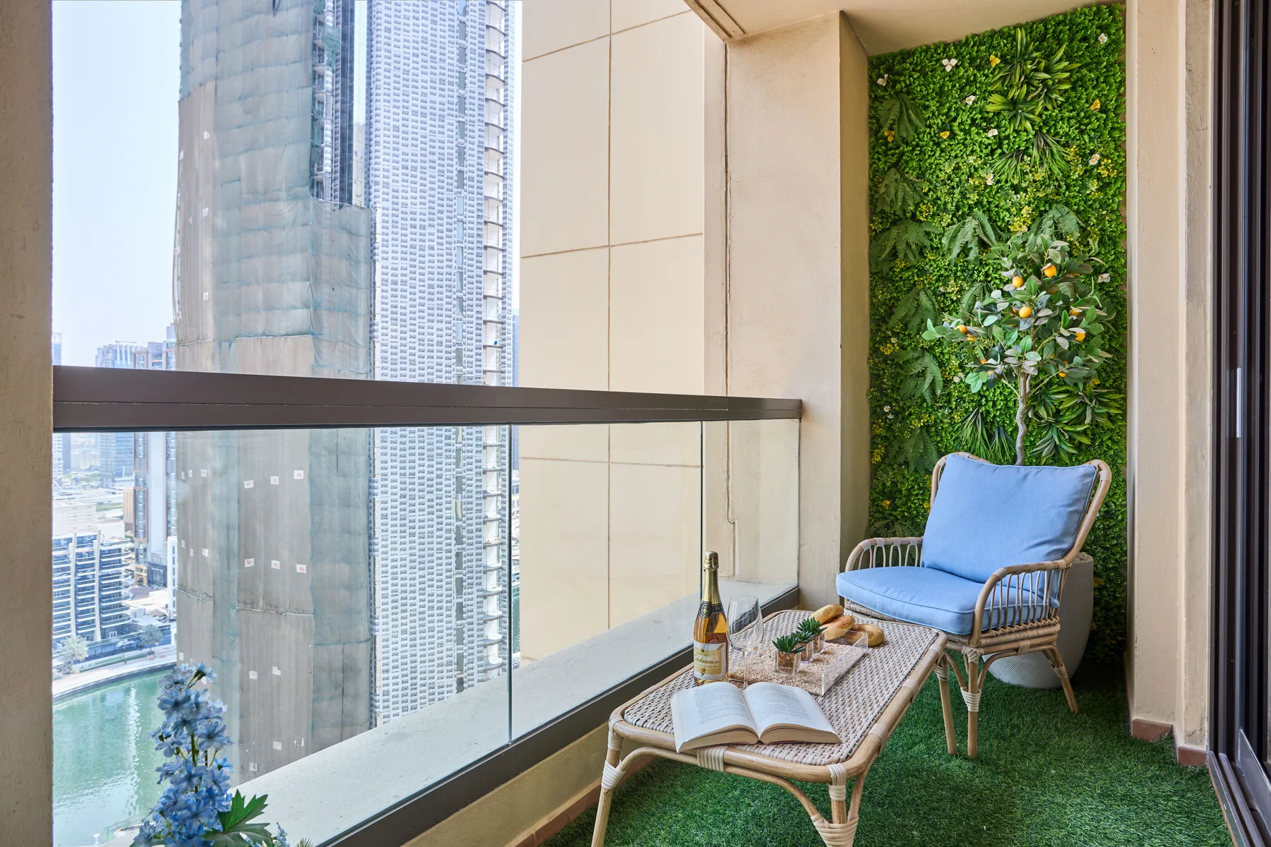 Una zona de estar en el balcón, con un sillón azul junto a una pared verde y vistas de la ciudad.