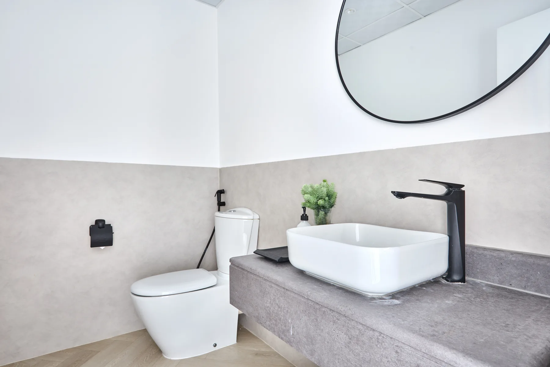 Un baño moderno con inodoro, lavabo sobre encimera y un gran espejo redondo.