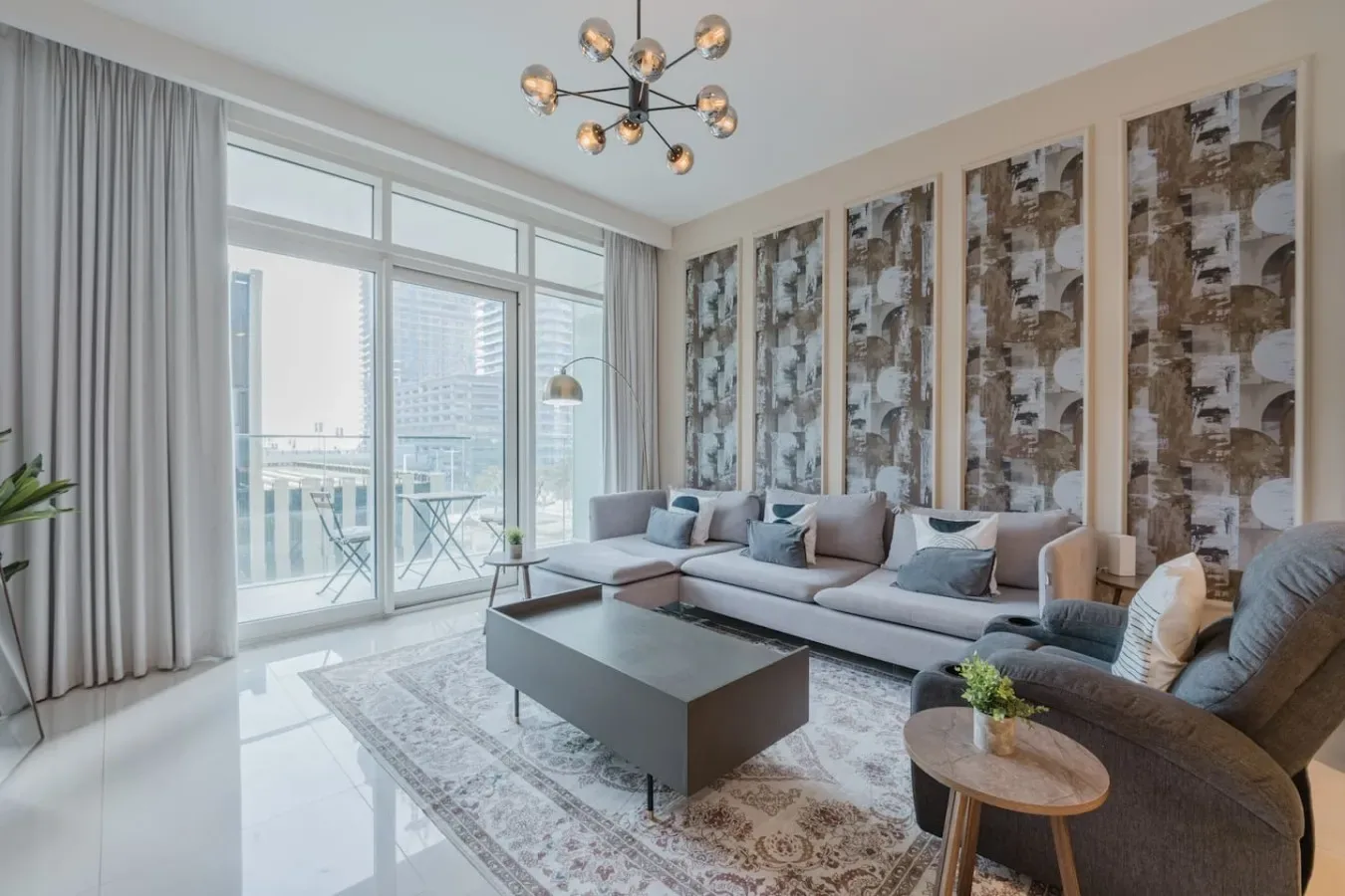 Una sala luminosa con sofá, sillón y grandes ventanales que dan a un balcón.