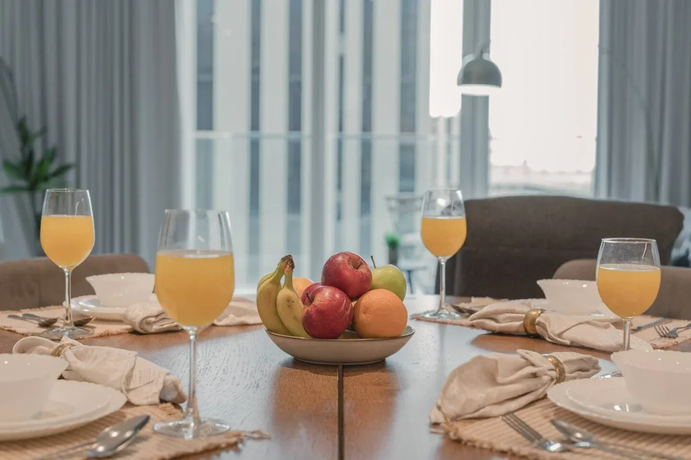 Una mesa de comedor está puesta con platos, vasos de jugo y un cuenco de fruta.