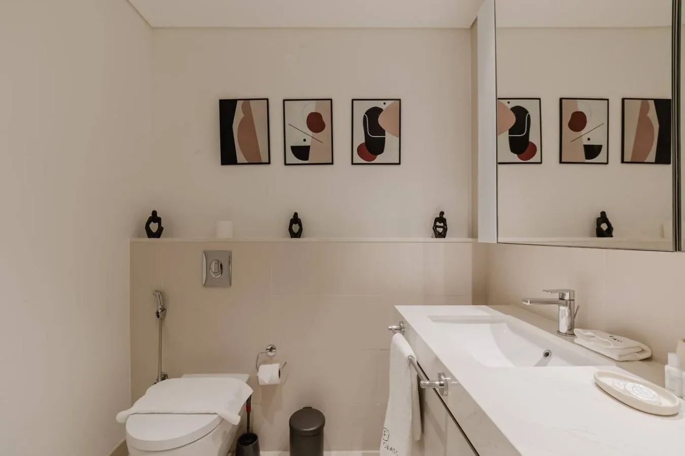 Un baño con un inodoro, una encimera larga con lavabo y arte abstracto enmarcado.