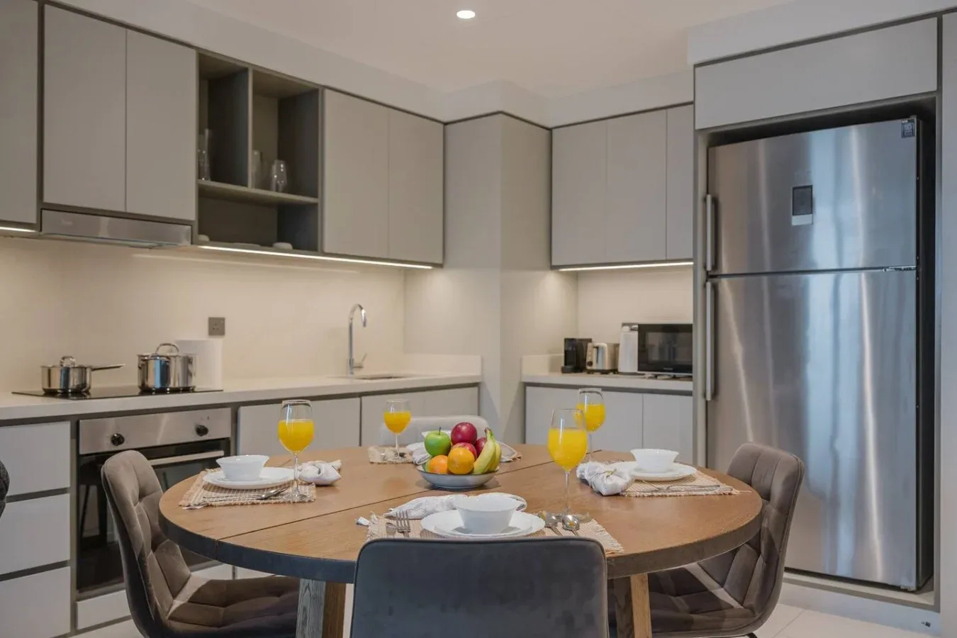 Una cocina moderna con una mesa ovalada puesta con platos y fruta.