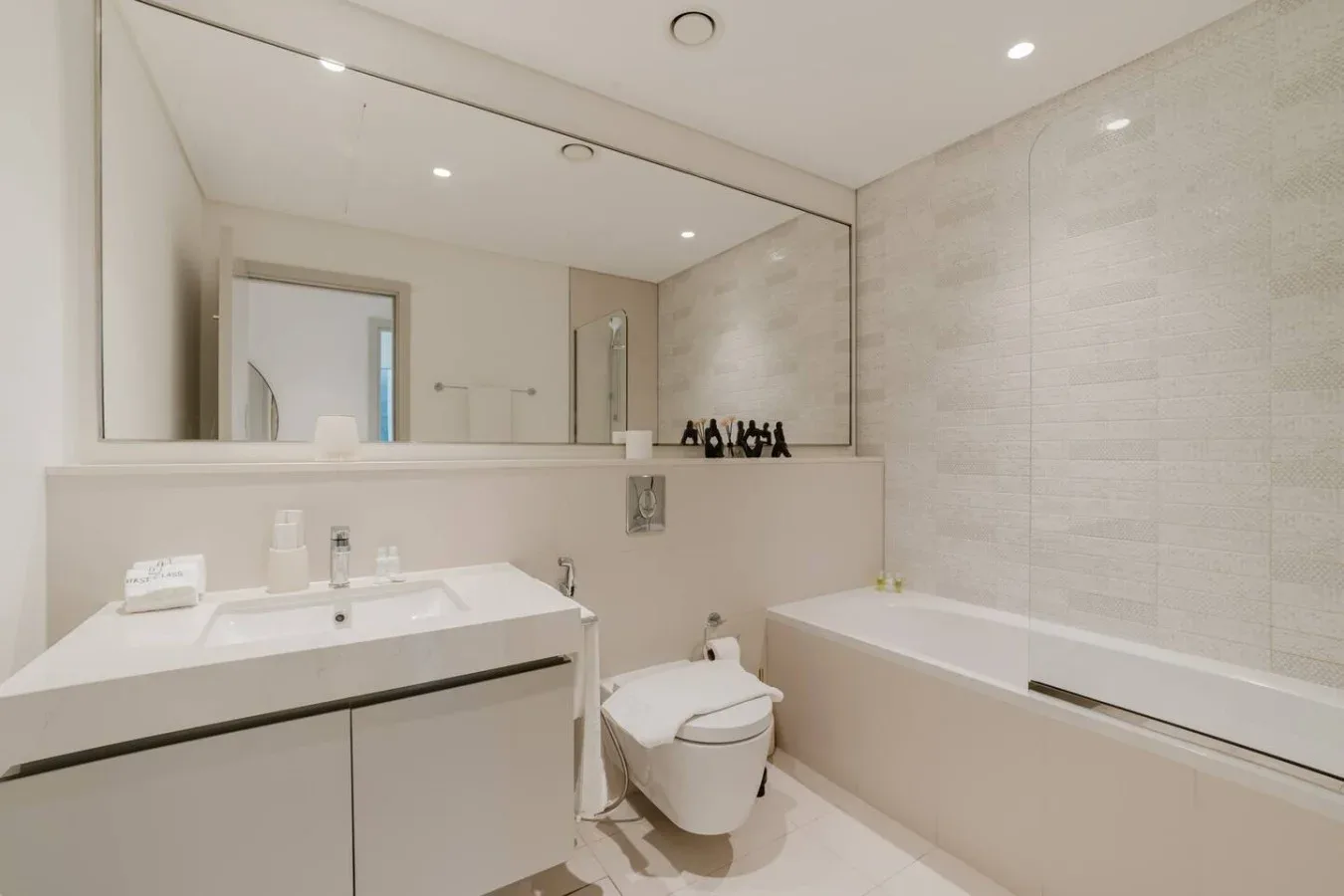 Un baño luminoso con lavabo, inodoro y bañera bajo un espejo grande.