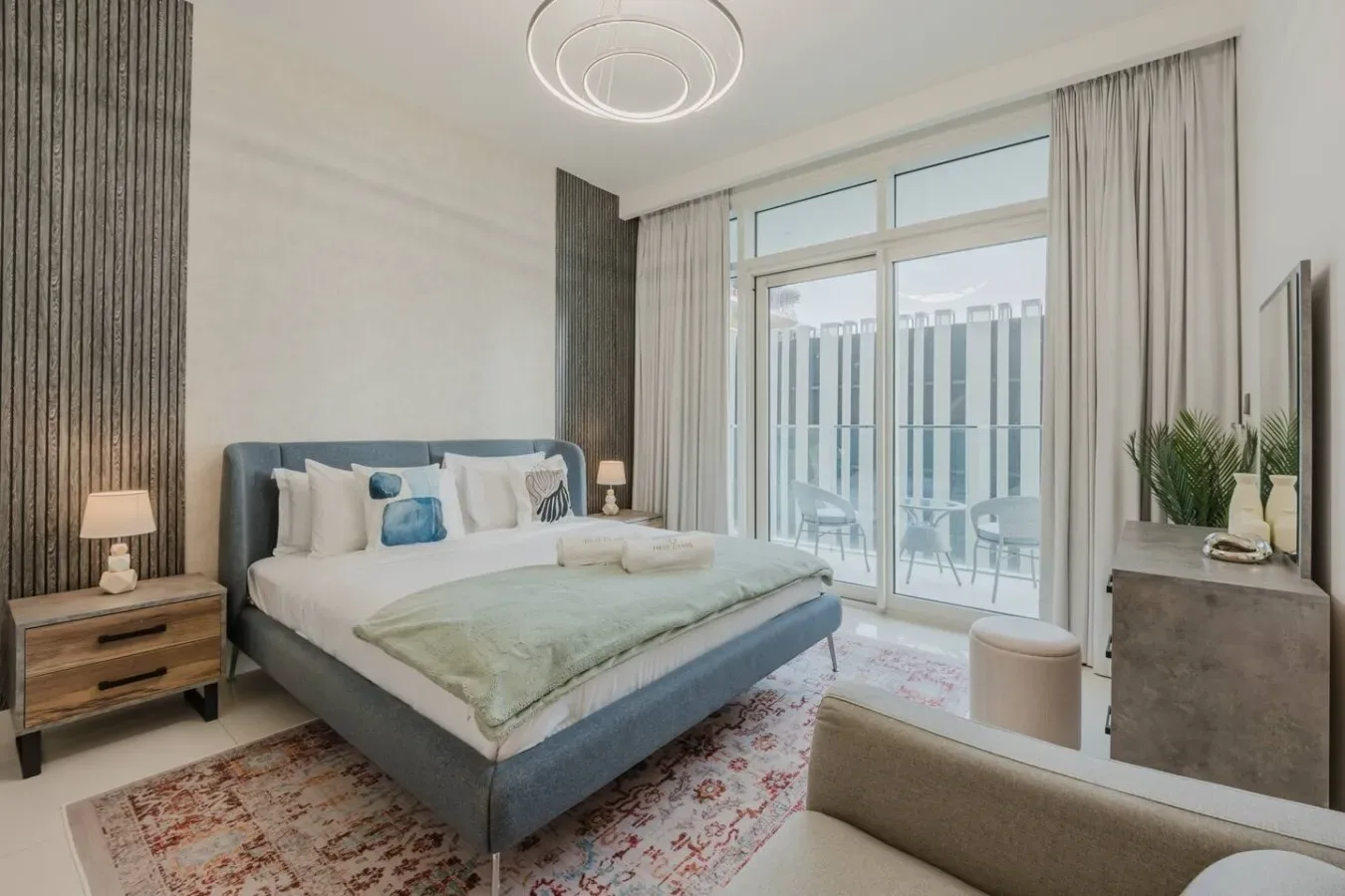A bedroom with a bed, bedside tables, and large windows opening onto a balcony.