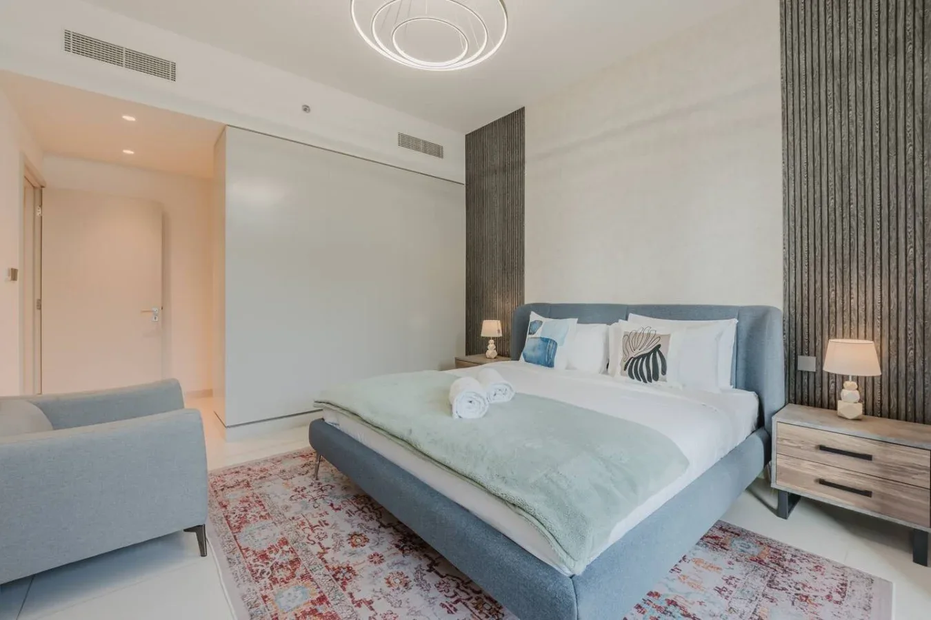 Dormitorio con una cama, ropa de cama clara y una alfombra estampada.
