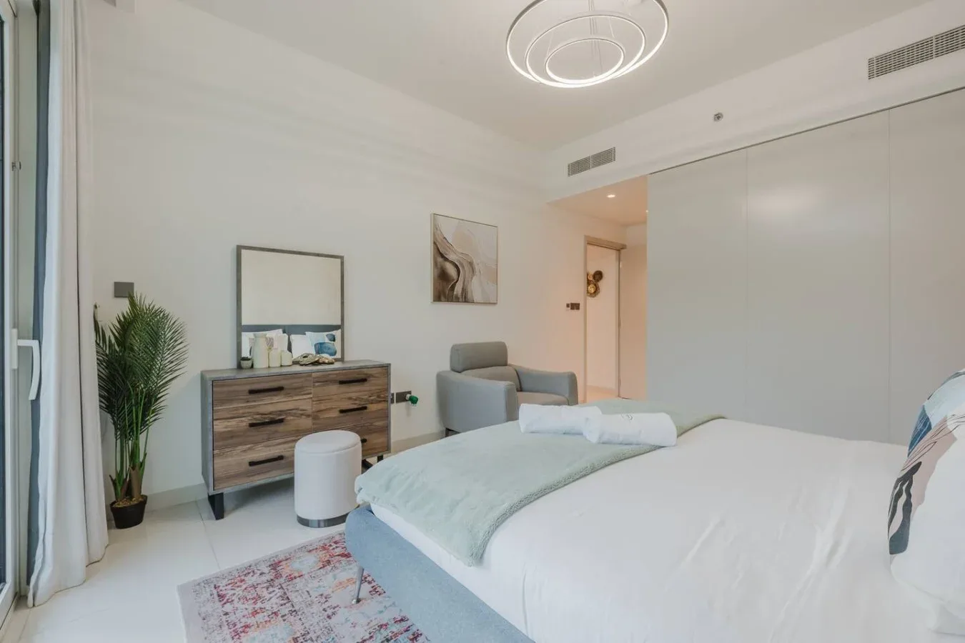 Un dormitorio luminoso con una cama bien tendida, una cómoda y un sillón.