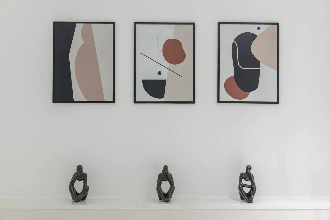 Tres láminas abstractas enmarcadas cuelgan sobre pequeñas esculturas en un estante blanco.