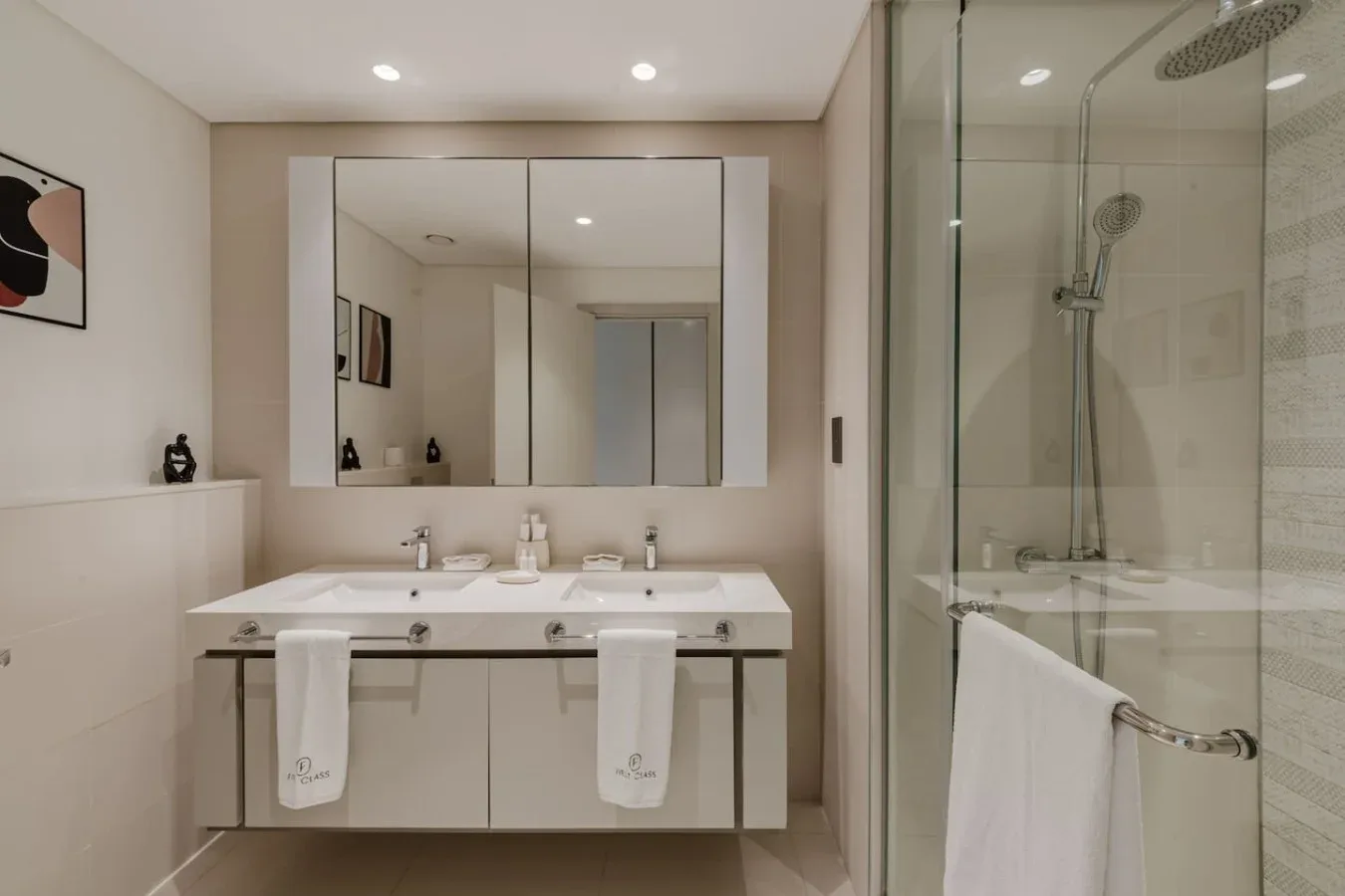 Un baño luminoso con lavabo doble y una ducha de cristal.