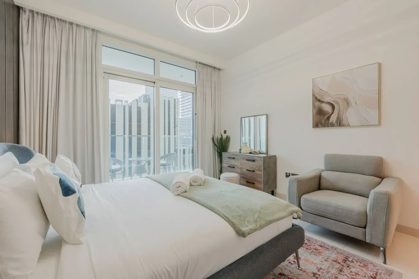 Un dormitorio luminoso con una cama, una ventana amplia y un sillón.