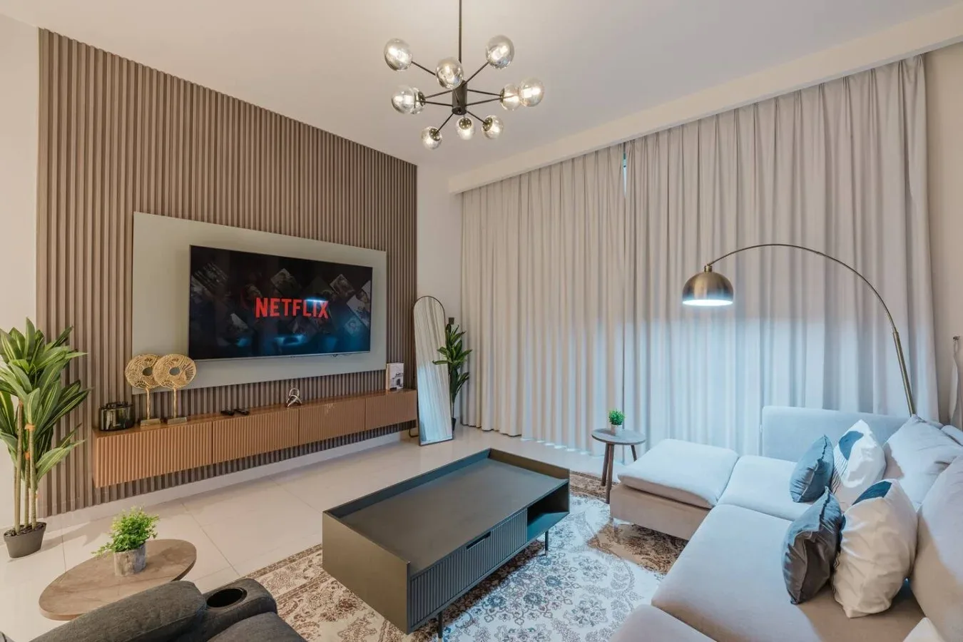 Una sala de estar moderna con una pared de televisión y asientos claros.