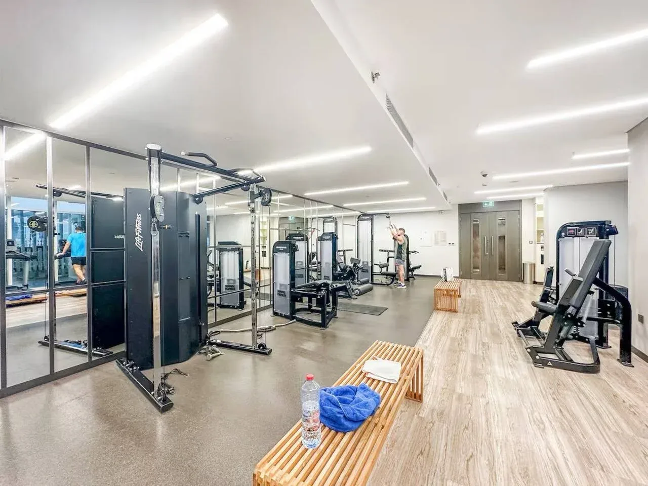 Un gimnasio con máquinas de ejercicio y un banco de madera en el espacio abierto.