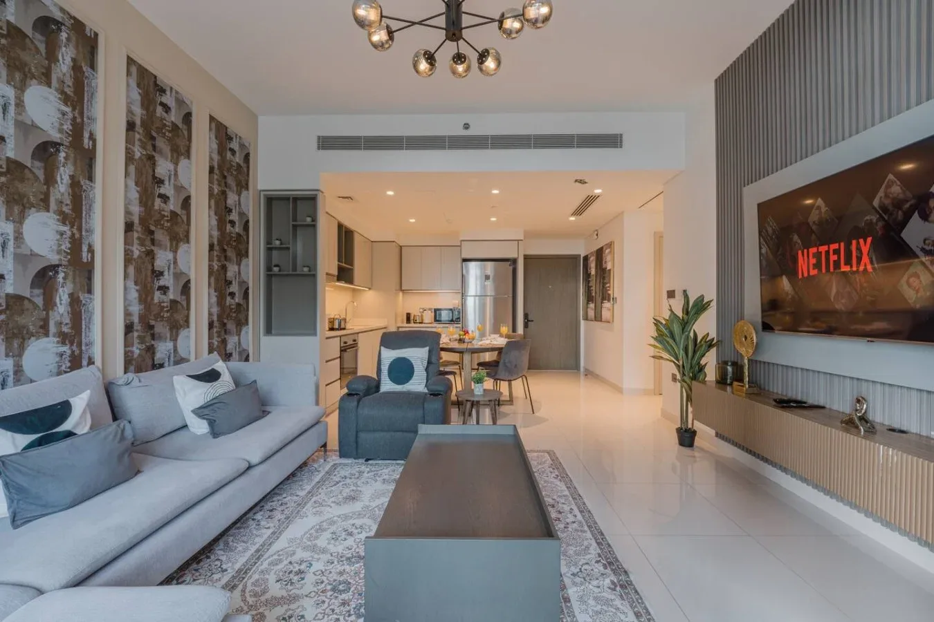 Una sala de estar moderna se abre a una cocina, con asientos frente a un televisor de pared.