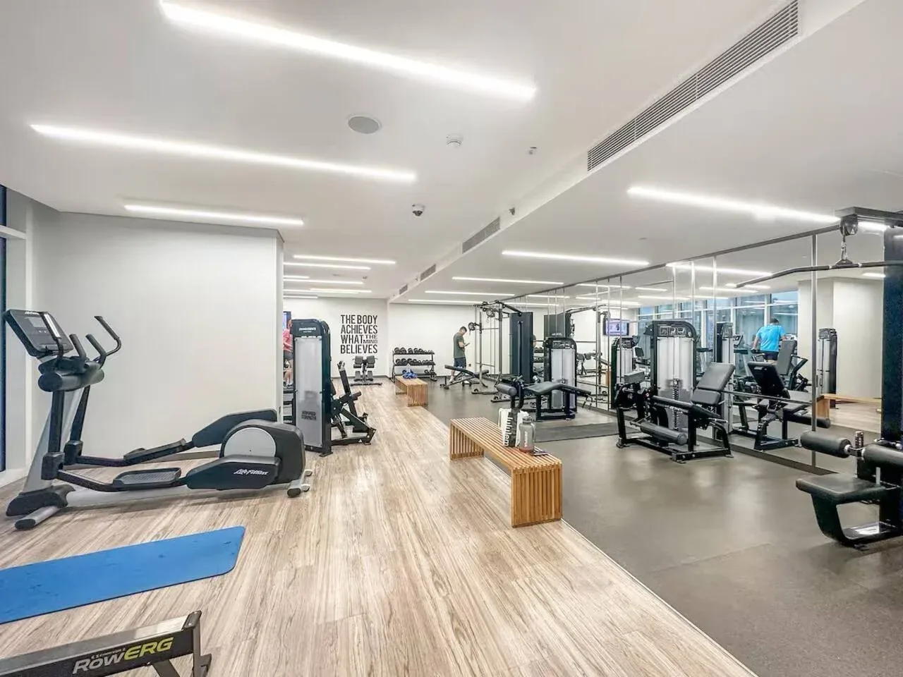 Un gimnasio luminoso con máquinas de ejercicio, pesas y paredes con espejos.