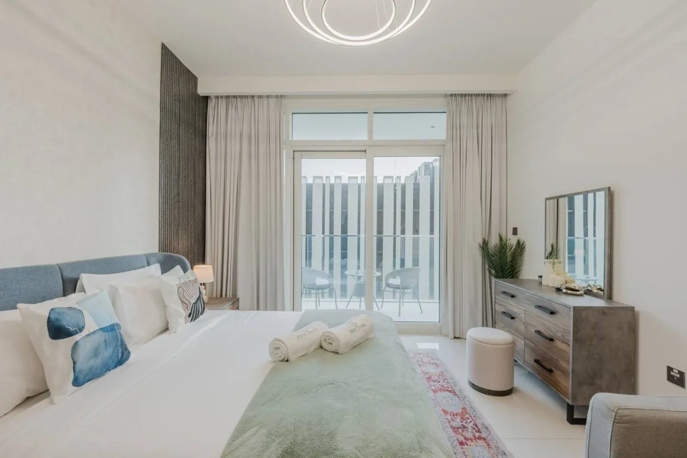 Un dormitorio luminoso con una cama, una mesita de noche y puertas de vidrio hacia el balcón.