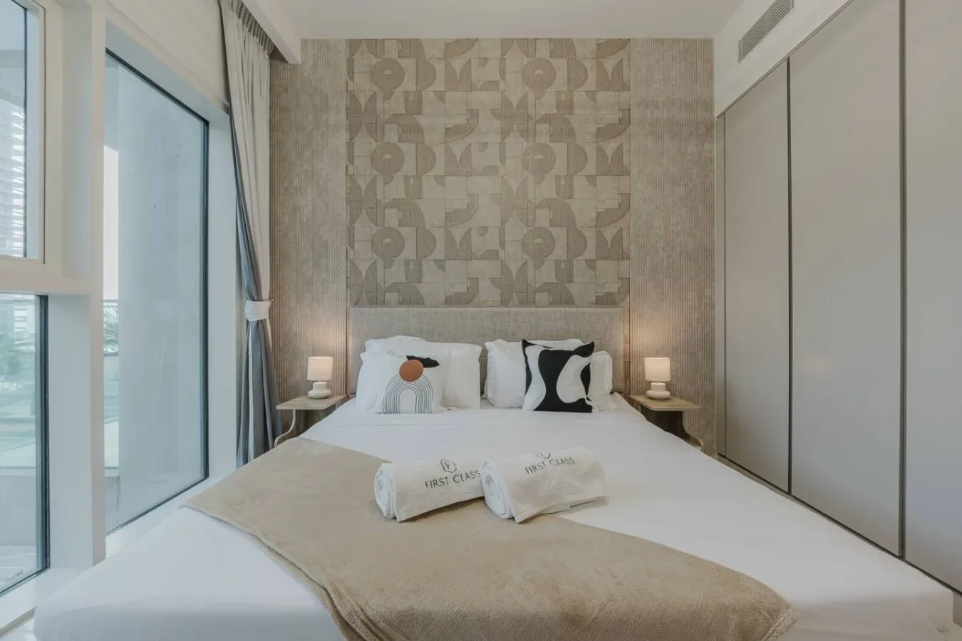 Un dormitorio con una cama tendida bajo una pared decorativa estampada.
