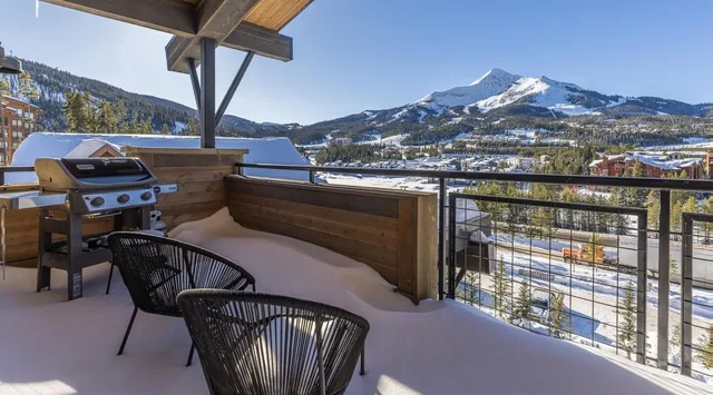 Una terraza exterior cubierta mira hacia un paisaje montañoso nevado, con asientos y una parrilla.