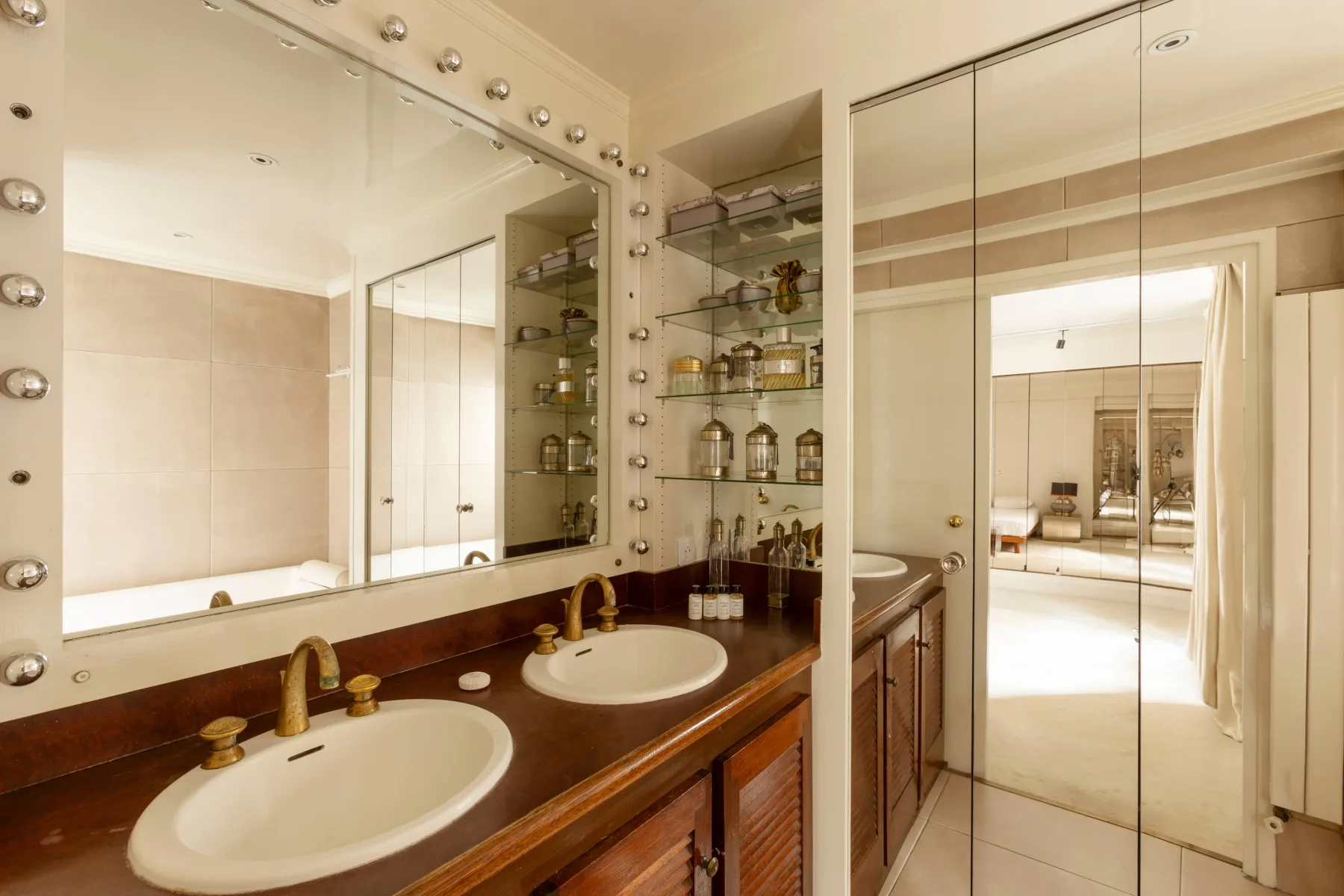 Un tocador de baño con dos lavabos, espejos y estantes abiertos.