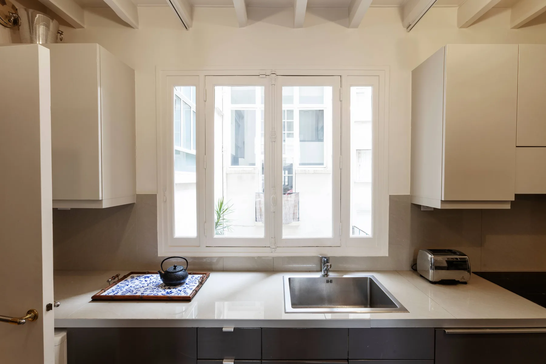 Una cocina luminosa con gabinetes blancos, una encimera y un fregadero bajo las ventanas.